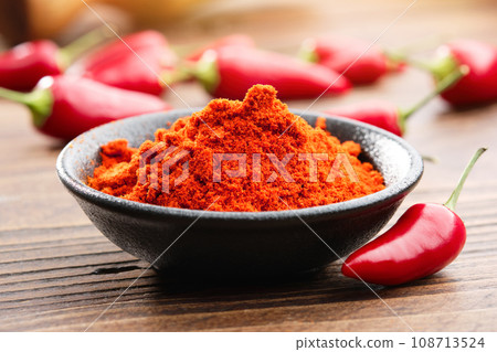 Bowl of red chili pepper ground to powder and whole red hot pepper pods on background. Bowl of red chili pepper ground to powder and whole red hot pepper pods on background. 108713524
