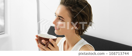 Close up portrait of relaxed woman, resting in bed, waking up and drinking morning cup of coffee, smiling with happy, pleased face Close up portrait of relaxed woman, resting in bed, waking up and drinking morning cup of coffee, smiling with happy, pleased face 108713744