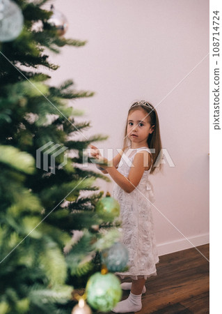 Pretty girl decorating Christmas tree with baubles Pretty girl decorating Christmas tree with baubles 108714724