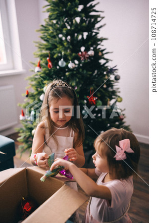 Sisters decorating Christmas tree with baubles and toys Sisters decorating Christmas tree with baubles and toys 108714725