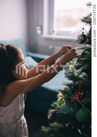 Pretty girl decorating Christmas tree with balls Pretty girl decorating Christmas tree with balls 108714726