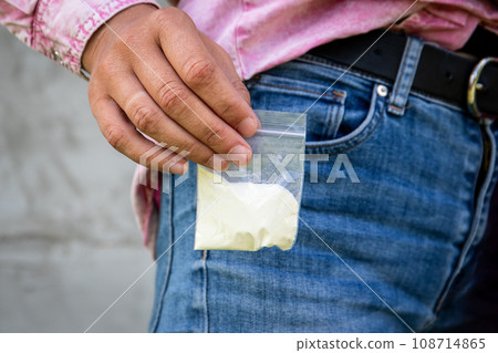 A bag of white powder taking out from the trouser pocket. Addiction and illegal trade A bag of white powder taking out from the trouser pocket. Addiction and illegal trade 108714865