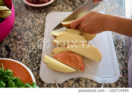 Closeup of the hands of a housewife chopping potato on a cutting board while preparing dinner in the home kitchen Closeup of the hands of a housewife chopping potato on a cutting board while preparing dinner in the home kitchen 108714995