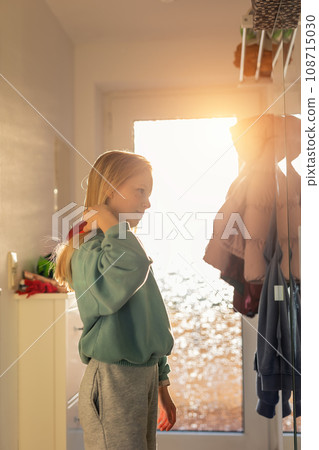 Cute happy 10 year little school girl child comb long blond hair with hairbrush near mirror against bright sun light in window at sunrise morning. Preteen independent kid prepare self go to school 108715030