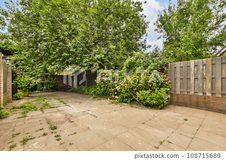 a backyard area with trees and flowers on the ground in front of an old brick fenced yard, surrounded by green foliage a backyard area with trees and flowers on the ground in front of an old brick fenced yard, surrounded by green foliage 108715689