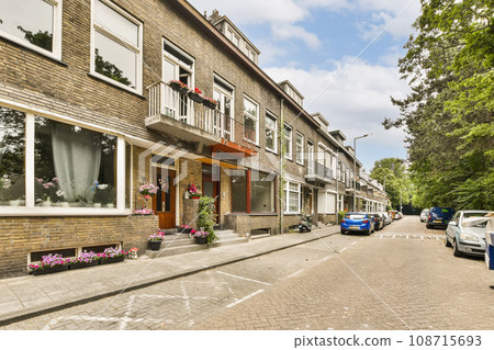 a city street with cars parked on the side and buildings in the back ground, some flowers are hanging from windows 108715693