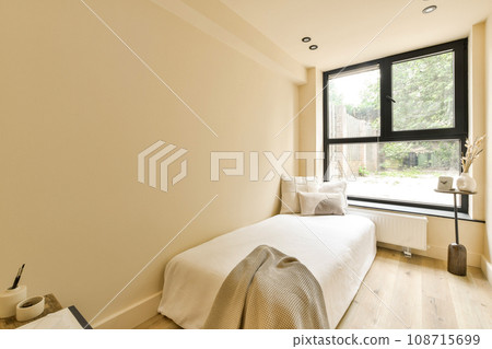 a bedroom with white walls and wood flooring, there is a small bed in the room has a blanket on it's headboard 108715699