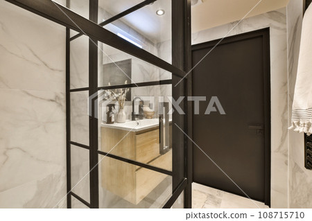 a bathroom with white marble walls and black trim around the shower door, which is open to reveal a large mirror 108715710