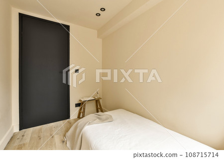 a room with a bed and a black door in the corner to the left is an empty chair on the right side 108715714