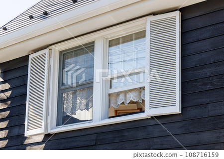 Black walled house with windows with white shutters and white lace curtains Black walled house with windows with white shutters and white lace curtains 108716159