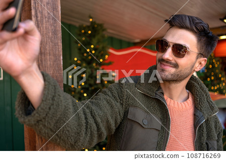Man wear sunglasses taking selfie near Christmas store 108716269