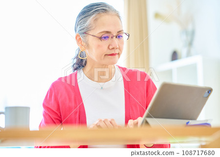 Senior woman operating a computer in her room Senior woman operating a computer in her room 108717680