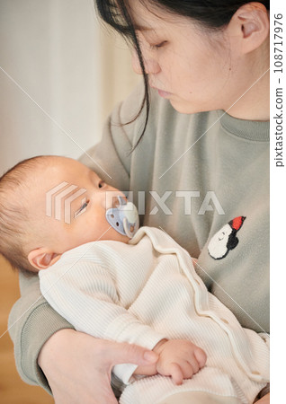 Baby sucking a pacifier, mother holding Baby sucking a pacifier, mother holding 108717976