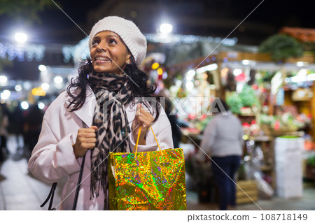 Cheerful hispanic woman with shopping bag at street Christmas market Cheerful hispanic woman with shopping bag at street Christmas market 108718149