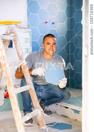 Cheerful man setting tile in bathroom Cheerful man setting tile in bathroom 108718369