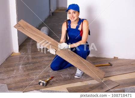 Professional female builder laying laminate flooring in room being renovated Professional female builder laying laminate flooring in room being renovated 108718471