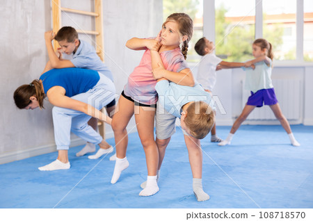 Children practicing in pair self-defence movements with female trainer supervision 108718570