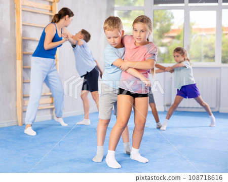 Boys and girls in gym perform basic elements of krav maga self-defense system. Boys and girls in gym perform basic elements of krav maga self-defense system. 108718616