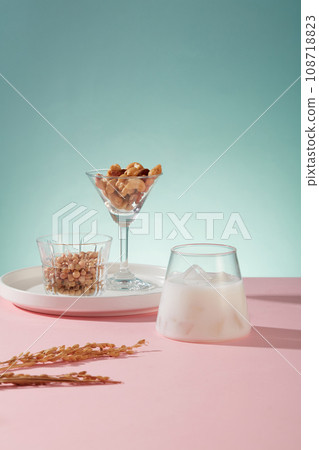 A cool glass of soy milk with ices arranged with raw mixed nuts and beans on pink surface. Eating nuts on a regular basis may improve your health in many ways A cool glass of soy milk with ices arranged with raw mixed nuts and beans on pink surface. Eating nuts on a regular basis may improve your health in many ways 108718823
