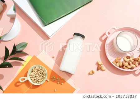 Flat lay of glass bottle of fresh milk arranged with soybeans, green leaves, mirror and a dish containing milk cup, almonds and cashew nuts. Organic healthy food Flat lay of glass bottle of fresh milk arranged with soybeans, green leaves, mirror and a dish containing milk cup, almonds and cashew nuts. Organic healthy food 108718837