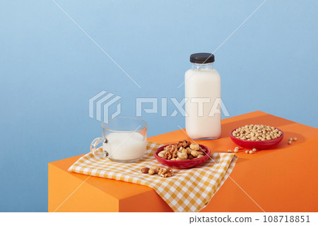 Red dishes with various types of nuts and beans arranged with an unbranded milk bottle on orange podium. All nuts have very similar macronutrient Red dishes with various types of nuts and beans arranged with an unbranded milk bottle on orange podium. All nuts have very similar macronutrient 108718851