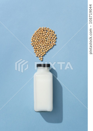 Unlabeled glass bottle of fresh milk decorated on blue background with a handful of soybeans. Soybeans can help maintain the elasticity of our skin Unlabeled glass bottle of fresh milk decorated on blue background with a handful of soybeans. Soybeans can help maintain the elasticity of our skin 108719044