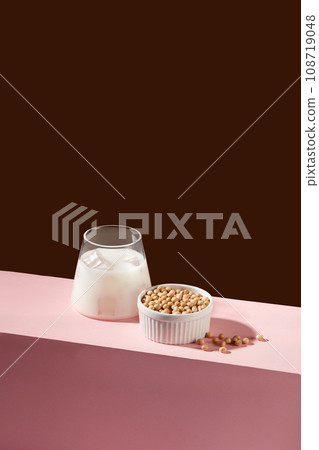 Minimal scene of a cup of fresh milk decorated with a lot of soybeans inside a white bowl. Nuts are a great source of several nutrients, including vitamin E Minimal scene of a cup of fresh milk decorated with a lot of soybeans inside a white bowl. Nuts are a great source of several nutrients, including vitamin E 108719048