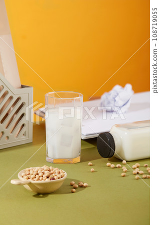 Concept of office desk with glass cup and bottle filled with soy milk. Soybeans contained in a ceramic bowl. Soy milk is made by simply blending water with soaked soybeans Concept of office desk with glass cup and bottle filled with soy milk. Soybeans contained in a ceramic bowl. Soy milk is made by simply blending water with soaked soybeans 108719055