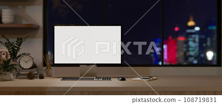 A computer monitor mockup on a wooden desk against the window with a city night light view. 108719831