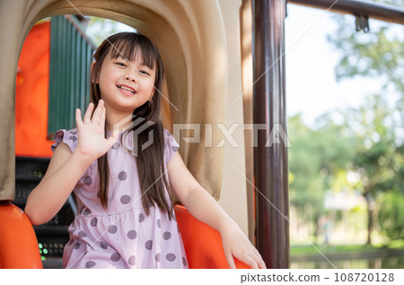 A cheerful and adorable young Asian girl is playing on a colorful slide in an outdoor playground. A cheerful and adorable young Asian girl is playing on a colorful slide in an outdoor playground. 108720128
