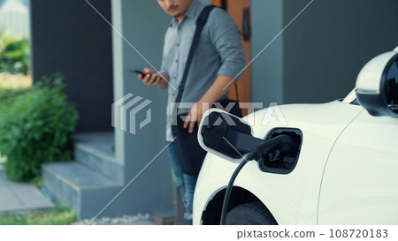 Progressive man unplugs the electric vehicle's charger at his residence. Progressive man unplugs the electric vehicle's charger at his residence. 108720183