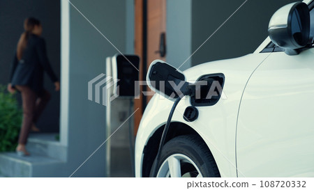 Progressive woman installing plug from home charging station to electric vehicle Progressive woman installing plug from home charging station to electric vehicle 108720332