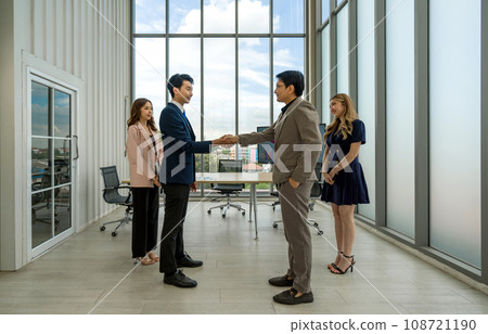 Corporate professional in formal attire engaged in a handshake during a meeting in a well-lit office space. Corporate professional in formal attire engaged in a handshake during a meeting in a well-lit office space. 108721190