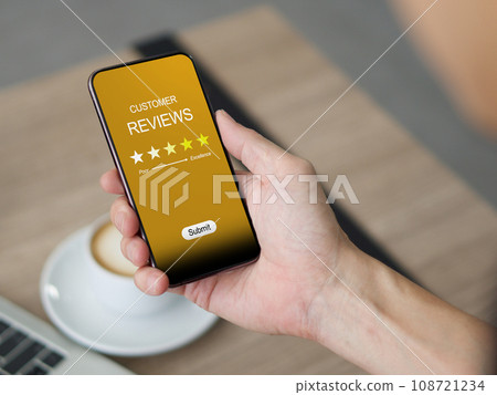Closeup hand holding a smartphone. The phone's screen shows a five star rating. 108721234