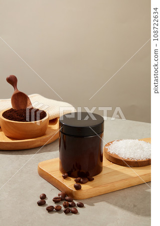 Advertising photo with cosmetic jar displayed on wooden trays with coffee beans, coffee powder and bath salt on gray background. Effective natural ingredients in exfoliating and caring for body skin 108722634