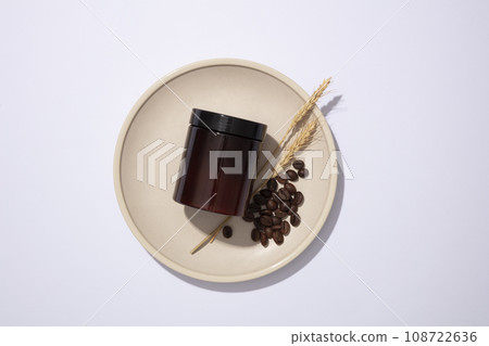 Top view of an amber plastic jar with coffee beans and ear of wheat placed on round ceramic dish on white background. Mockup scene, advertising photo for cosmetic of coffee ingredient Top view of an amber plastic jar with coffee beans and ear of wheat placed on round ceramic dish on white background. Mockup scene, advertising photo for cosmetic of coffee ingredient 108722636