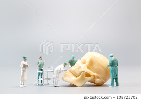 Miniature people Doctor with a giant human skull on a grey background Miniature people Doctor with a giant human skull on a grey background 108723702