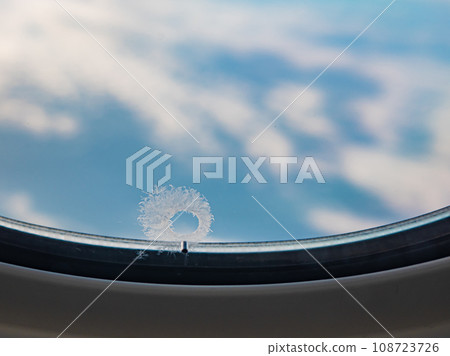 Tiny window hole with ice crystal, A close up of small bleed hole on airplane window when flying in the sky. Tiny window hole with ice crystal, A close up of small bleed hole on airplane window when flying in the sky. 108723726