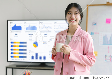 Portrait of smiling confident businesswoman standing and enjoying coffee in a meeting room. 108724255