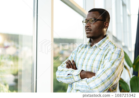 Portrait of thoughtful young african man in glasses standing near the window Portrait of thoughtful young african man in glasses standing near the window 108725342