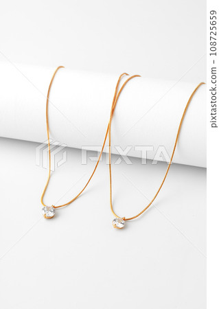 Two golden necklaces with diamond pendant on paper background 108725659