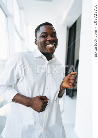 Young african man in white shirt and glasses posing near large window 108725716