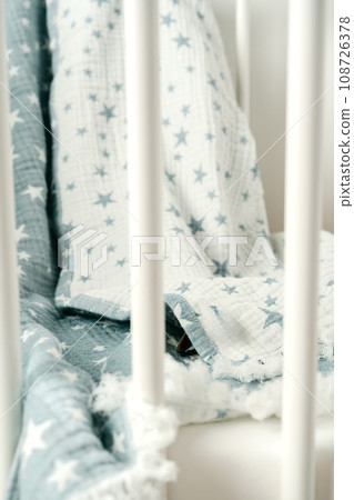 Soft blue muslin blanket hanging on a baby's bed 108726378