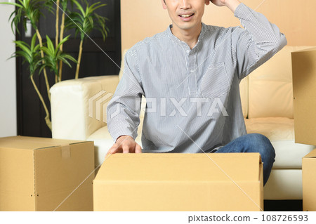 A young Asian man holding his head in front of a large number of cardboard boxes 108726593