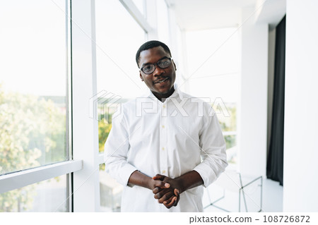 Young african man in white shirt and glasses posing near large window 108726872