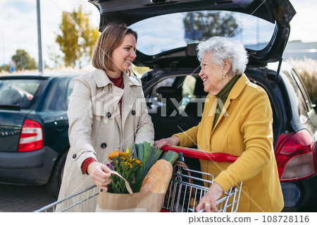 Mature granddaughter helping grandmother load groceries in to the car. Senior woman shopping at the shopping center. Mature granddaughter helping grandmother load groceries in to the car. Senior woman shopping at the shopping center. 108728116