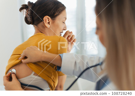 Doctor listening girl's breathing, heartbeats using a stethoscope. Teenage girl visiting paediatrician for annual preventive physical examination. Concept of preventive health care for adolescents Doctor listening girl's breathing, heartbeats using a stethoscope. Teenage girl visiting paediatrician for annual preventive physical examination. Concept of preventive health care for adolescents 108728240