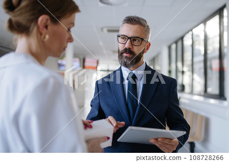 Pharmaceutical sales representative talking with female doctor in medical building. Hospital director consulting with healthcare staff. 108728266