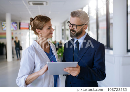 Pharmaceutical sales representative talking with female doctor in medical building. Hospital director consulting with healthcare staff. Pharmaceutical sales representative talking with female doctor in medical building. Hospital director consulting with healthcare staff. 108728283