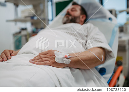 Patient with IV cannula in vein, hand lying in hospital bed. Man in intensive care unit in hospital. IV or intravenous therapy for the overweight man. 108728320